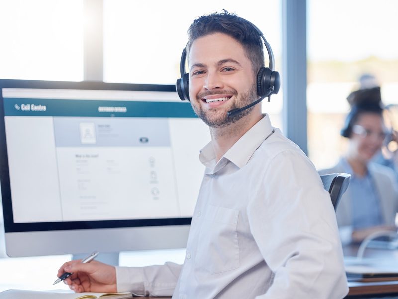 Man at call center, contact us with customer service employee, smile and CRM with consultant in workspace. Professional, portrait and communication, male with headset with help desk and telemarketing